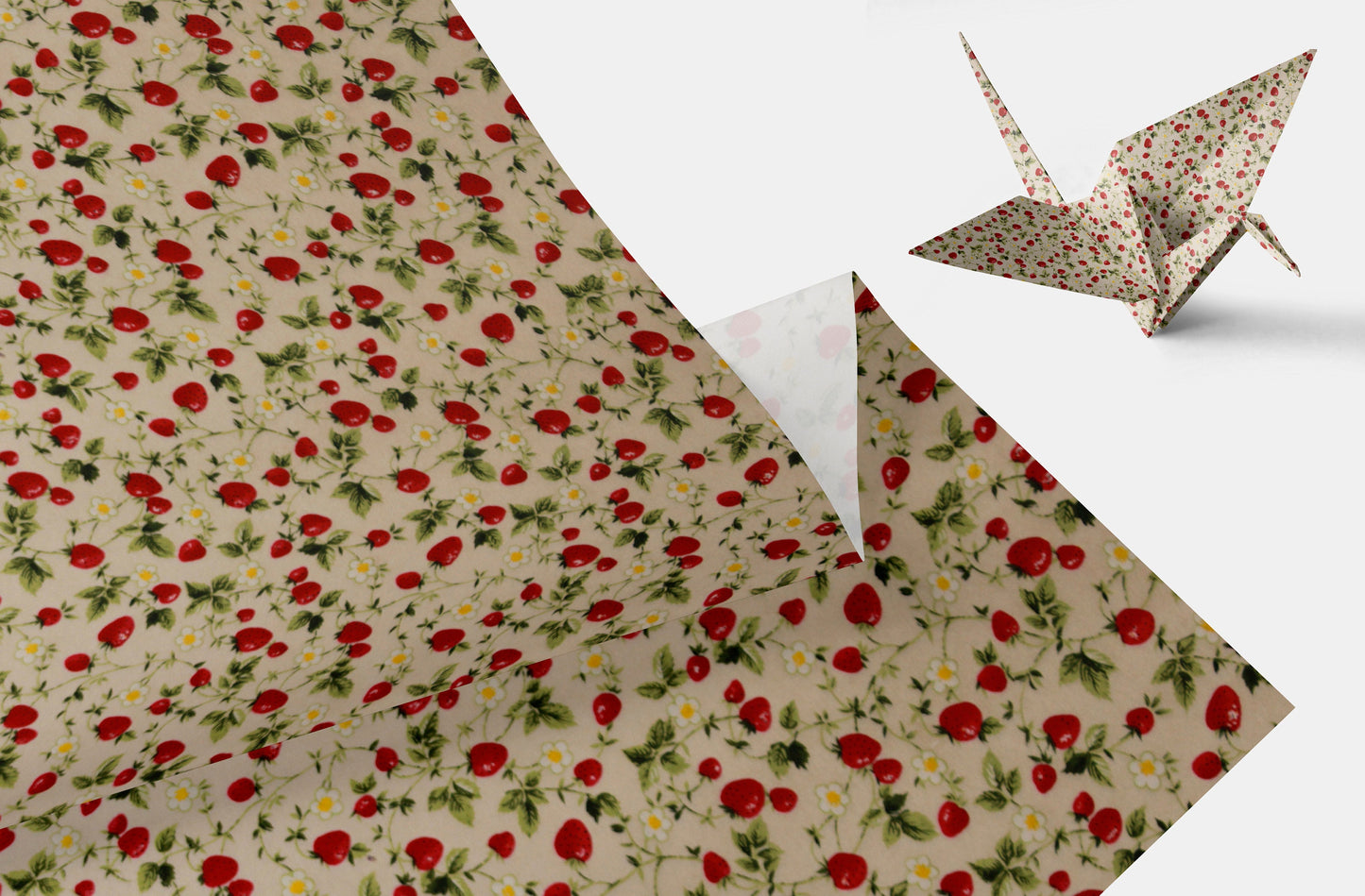 Pattern of red strawberries and green leaves on a beige background with a folded paper crane on a white background