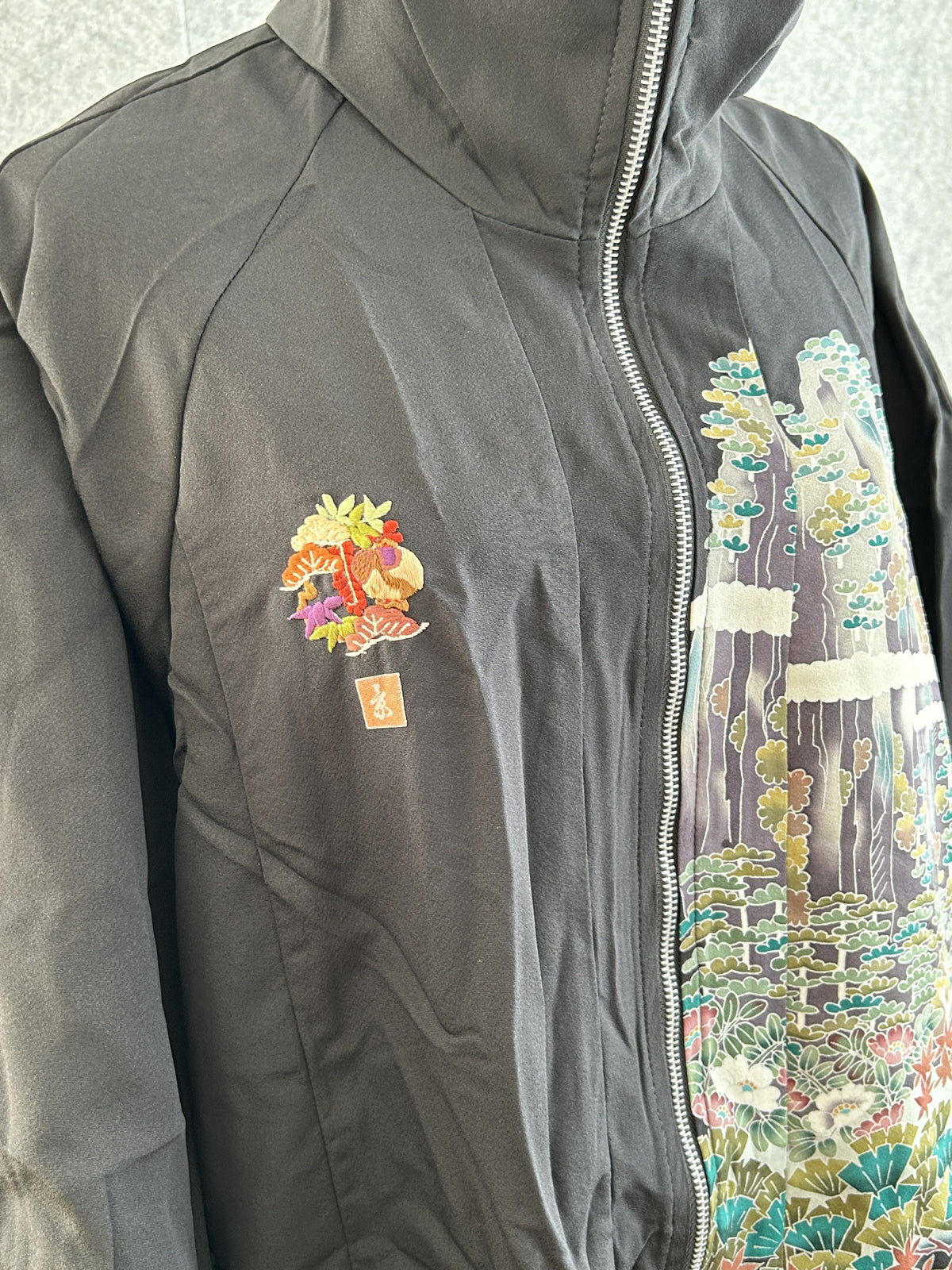 Black high collar kimono jacket with landscape scene, detail of small chest emblem