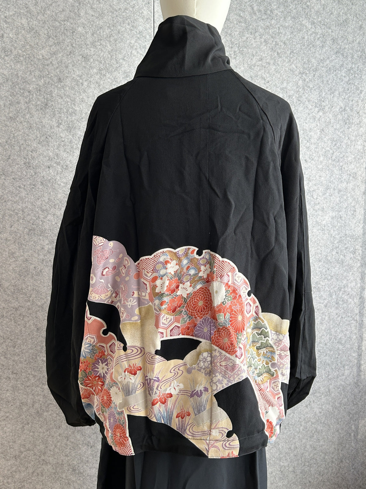 Black high collar kimono jacket with colourful panel at hem, back view
