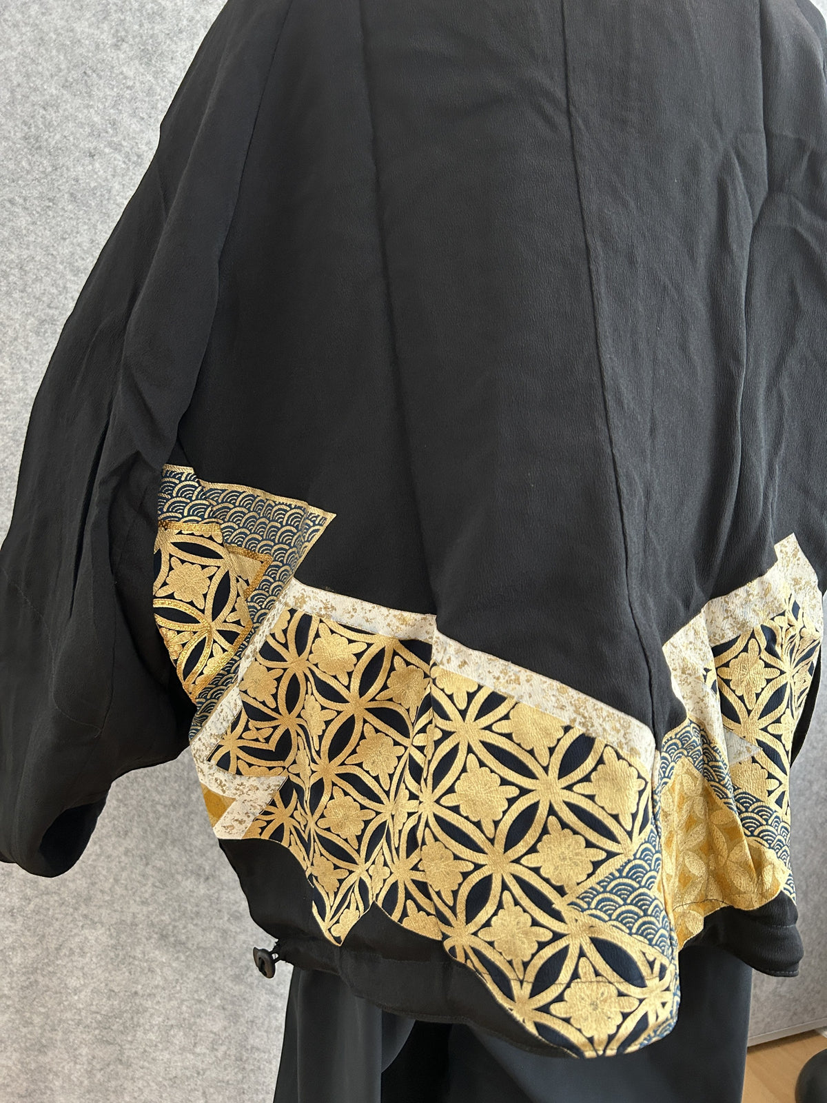 Black kimono jacket, detail of gold geometric hem panel, side view