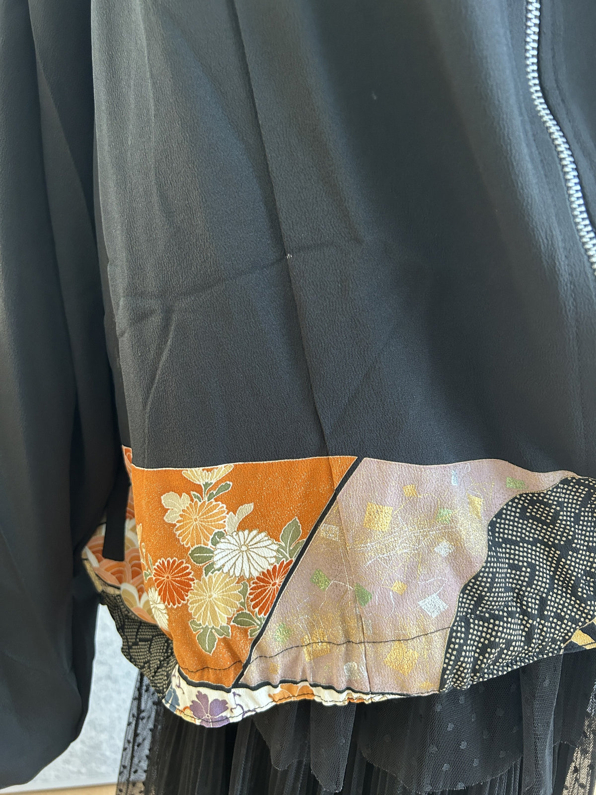 Black kimono jacket hem with orange floral band and zipper, detail