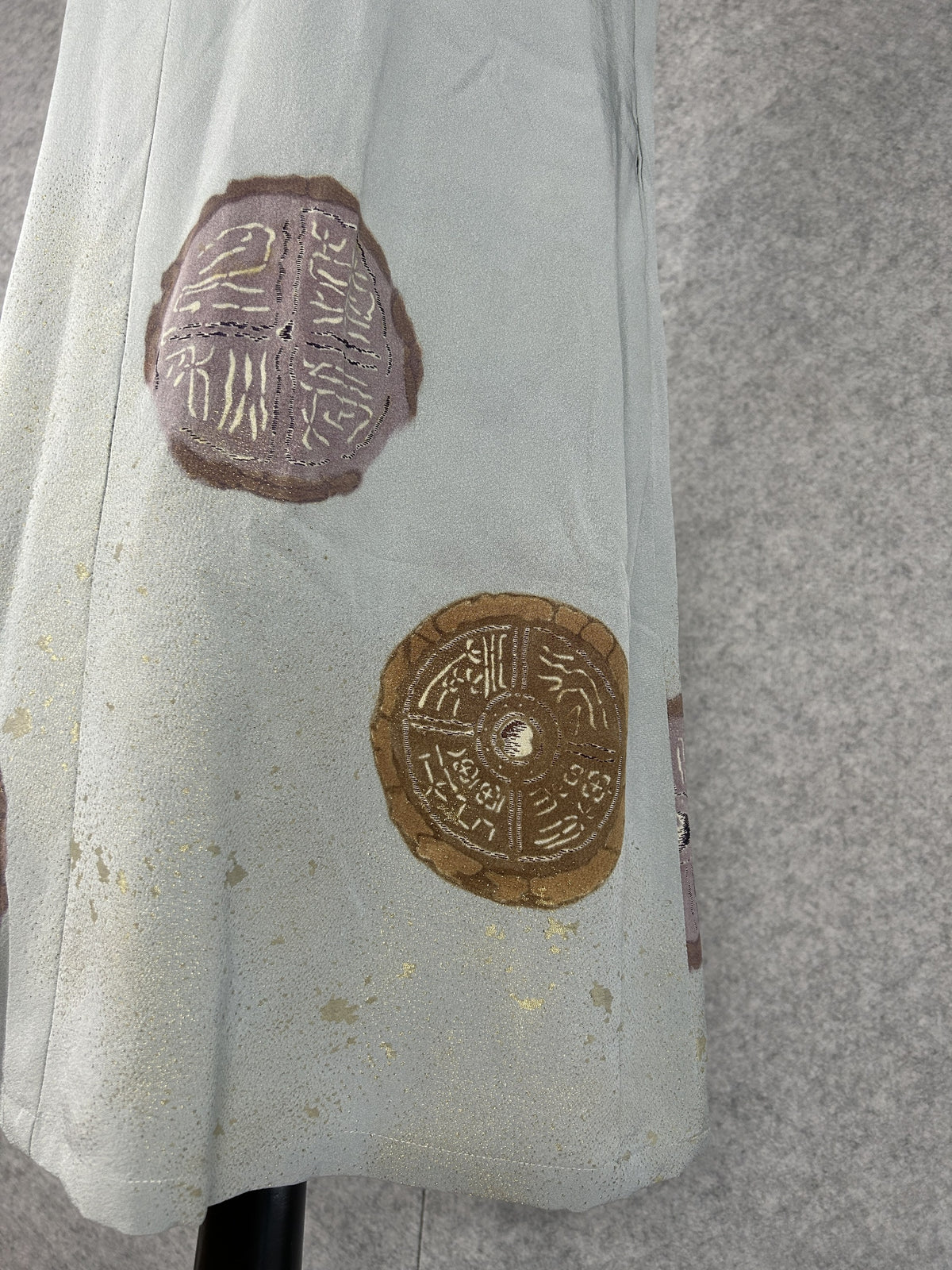 Detail of mauve and bronze round medallions with gold characters on sage silk