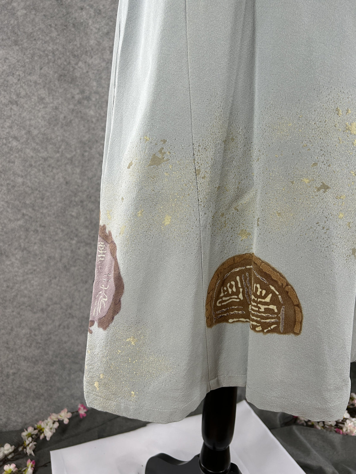 Hem of sage green kimono dress with bronze medallion and gold flecks