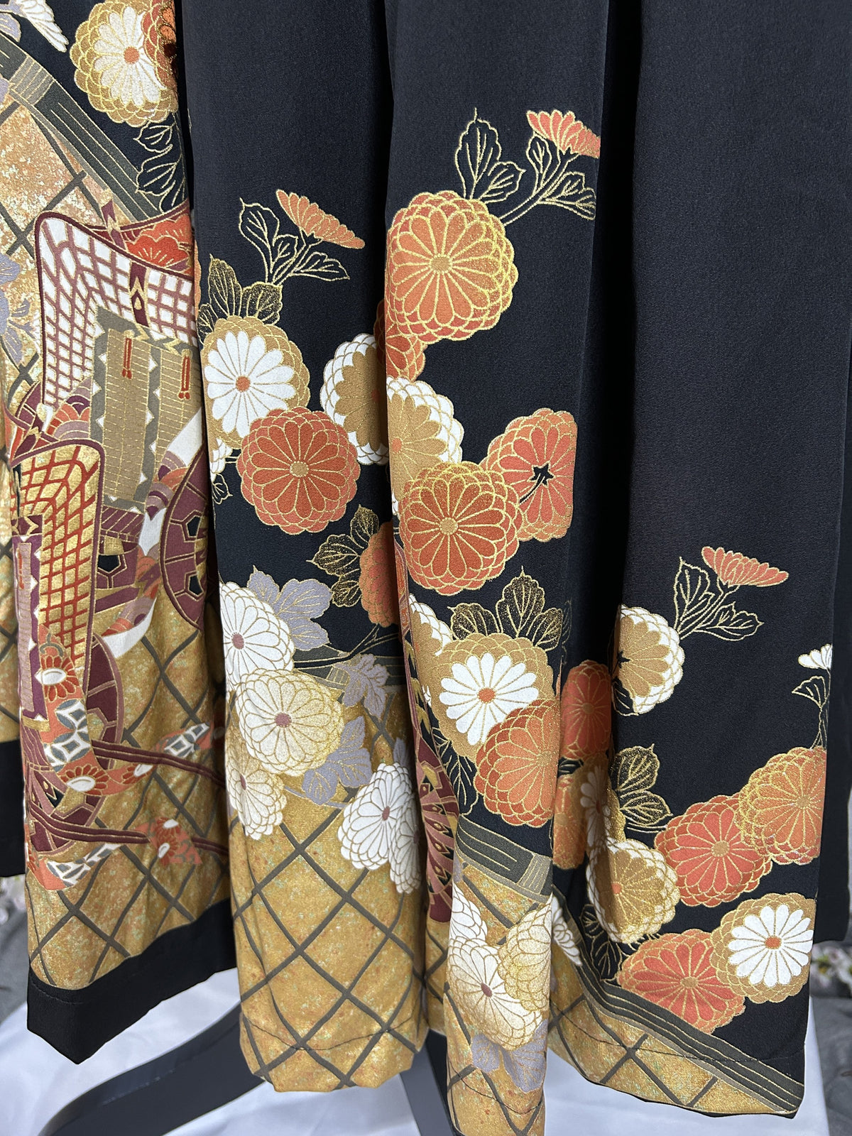 Black upcycled tomesode kimono hakama pants with orange and gold chrysanthemums, back view of the pleated hem