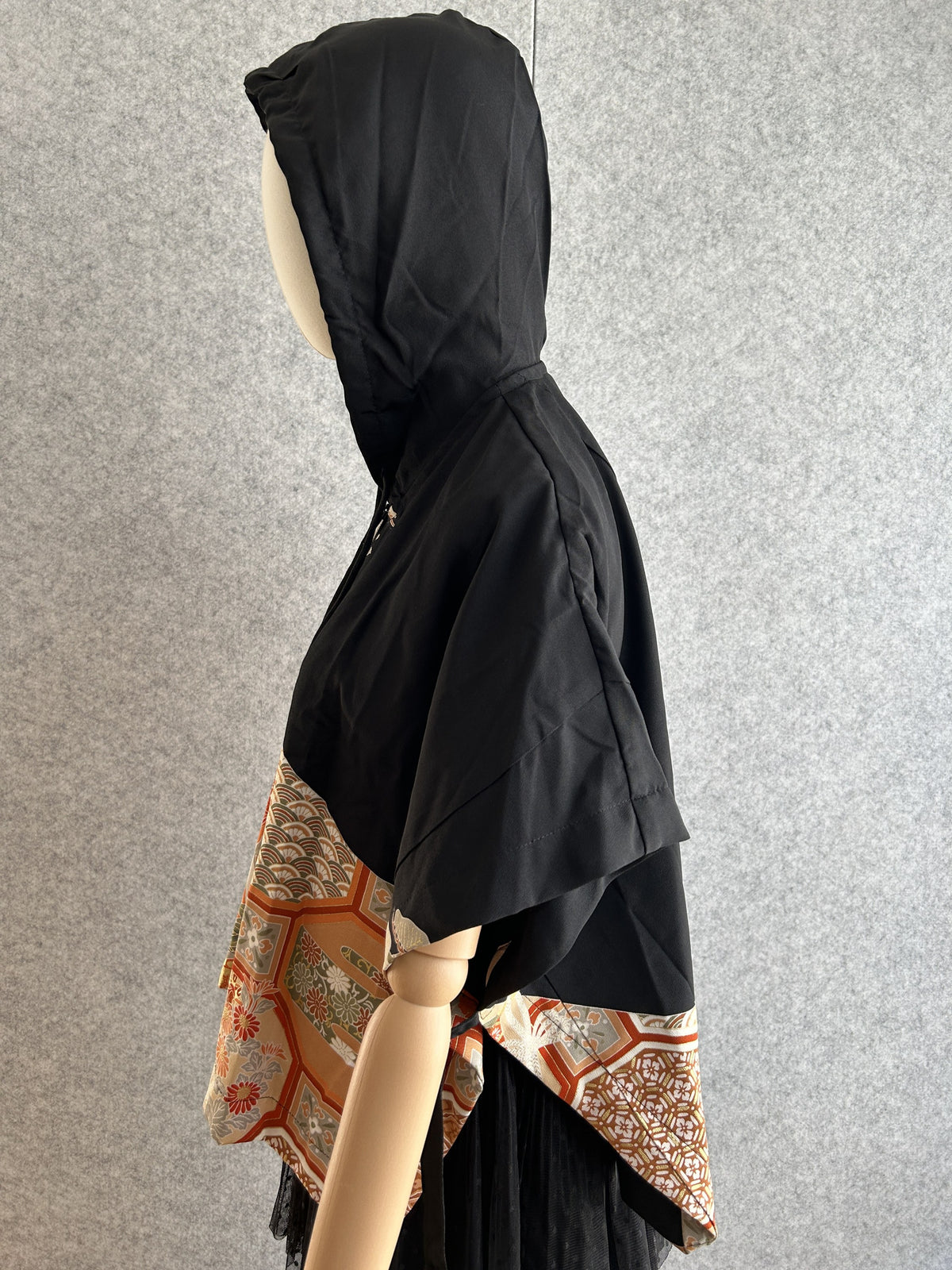 Black hooded kimono poncho with orange patterned hem, side view