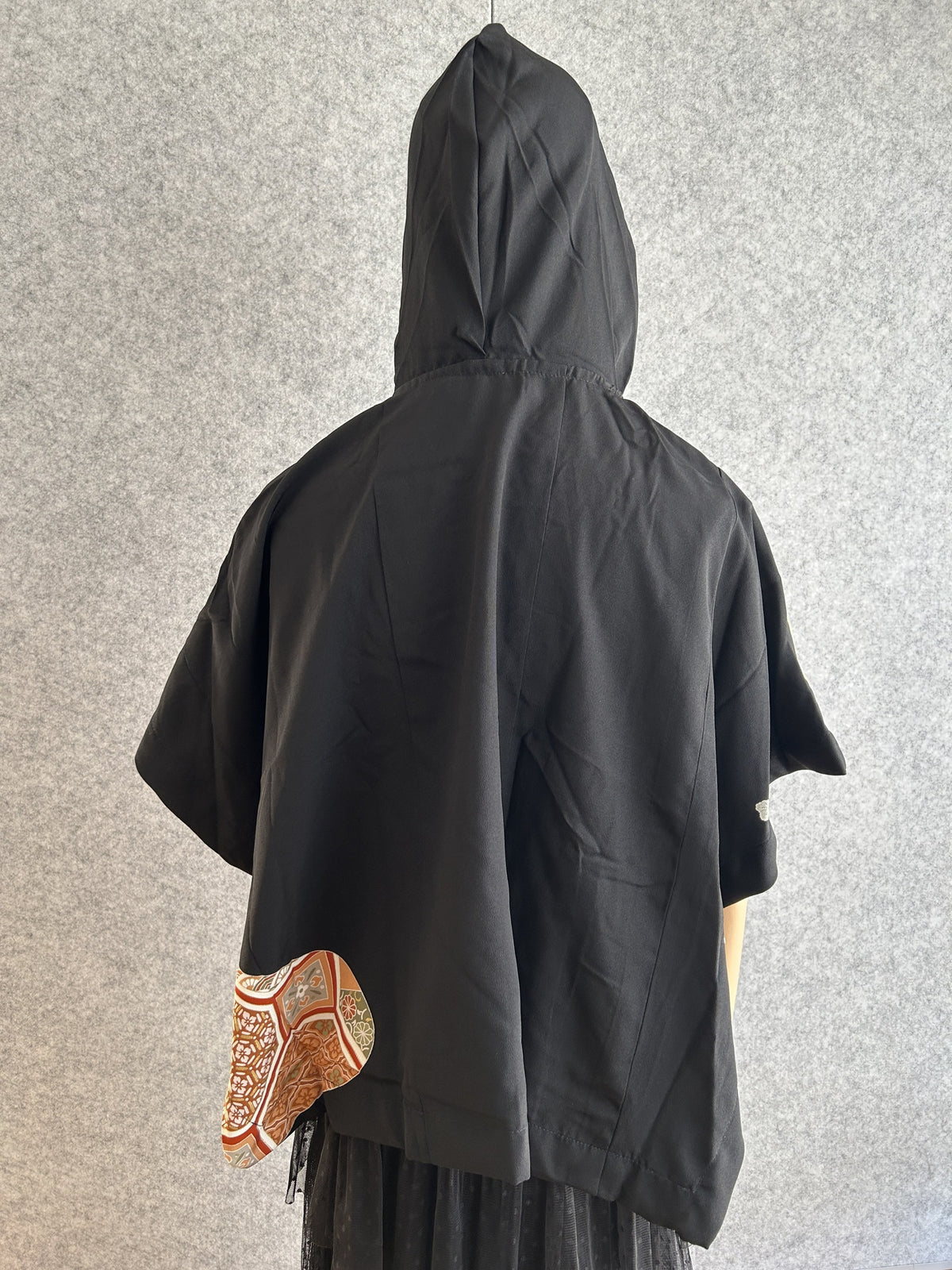 Black hooded kimono poncho with small patterned corner, back view
