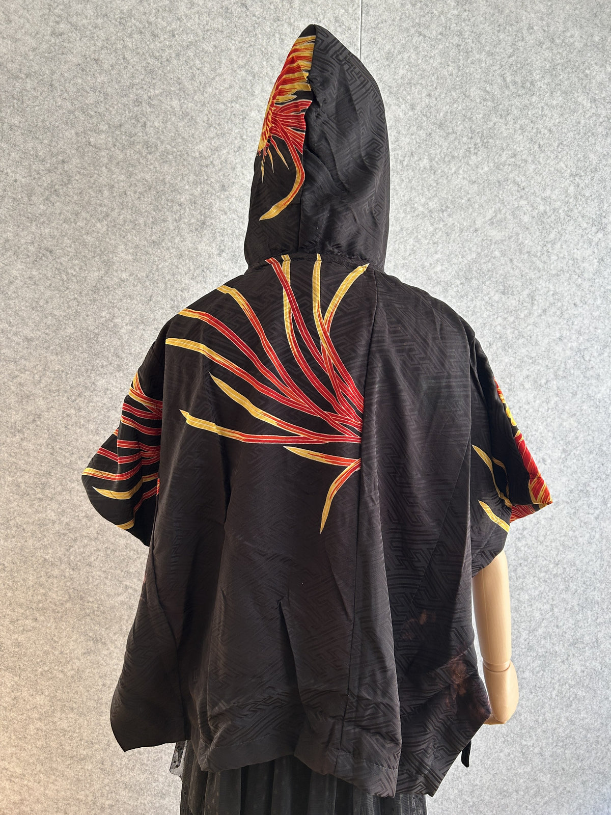 Black hooded kimono poncho with yellow and red feather motif, back view