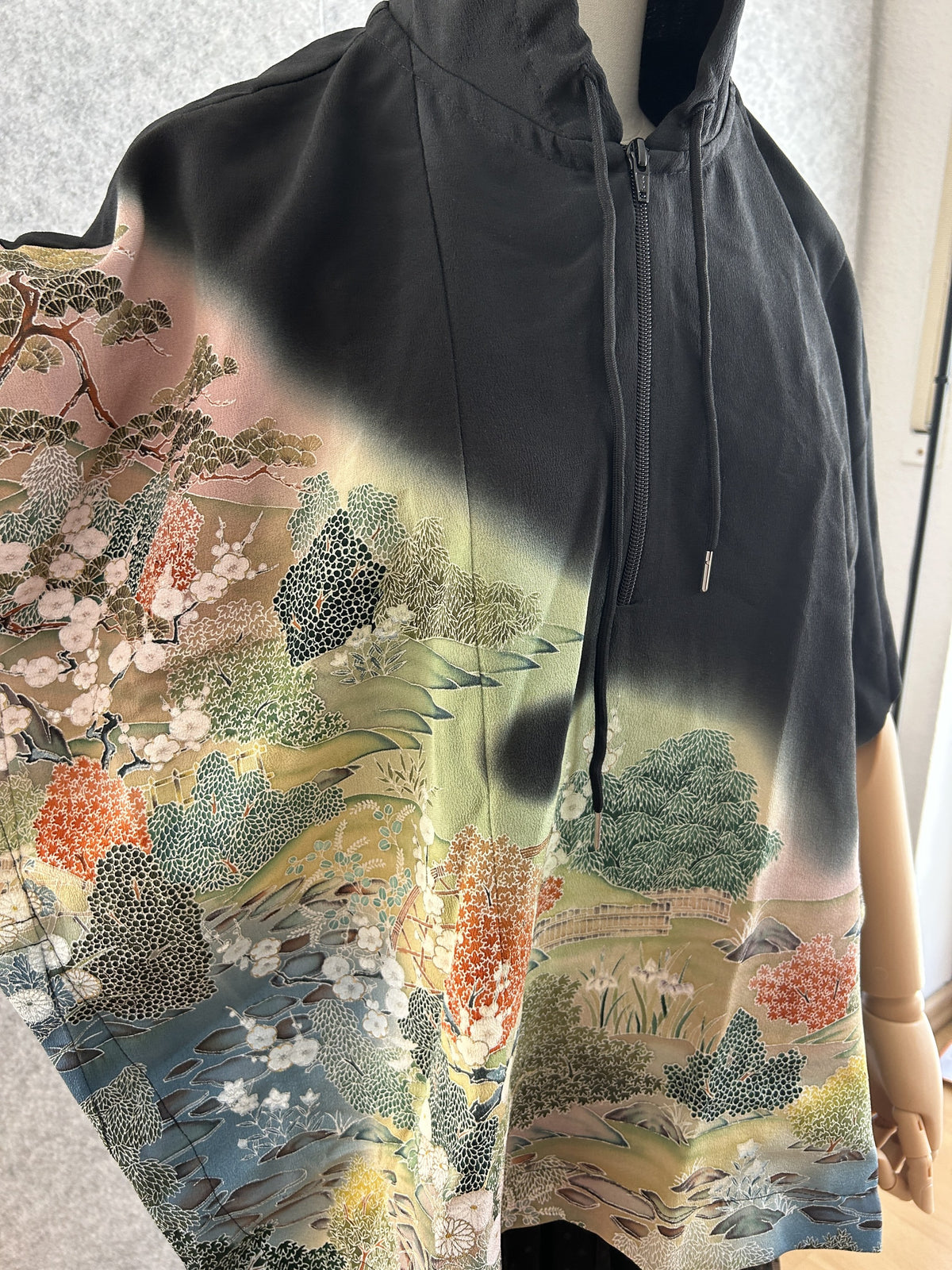 Black hooded kimono poncho, detail of landscape with trees and zipper
