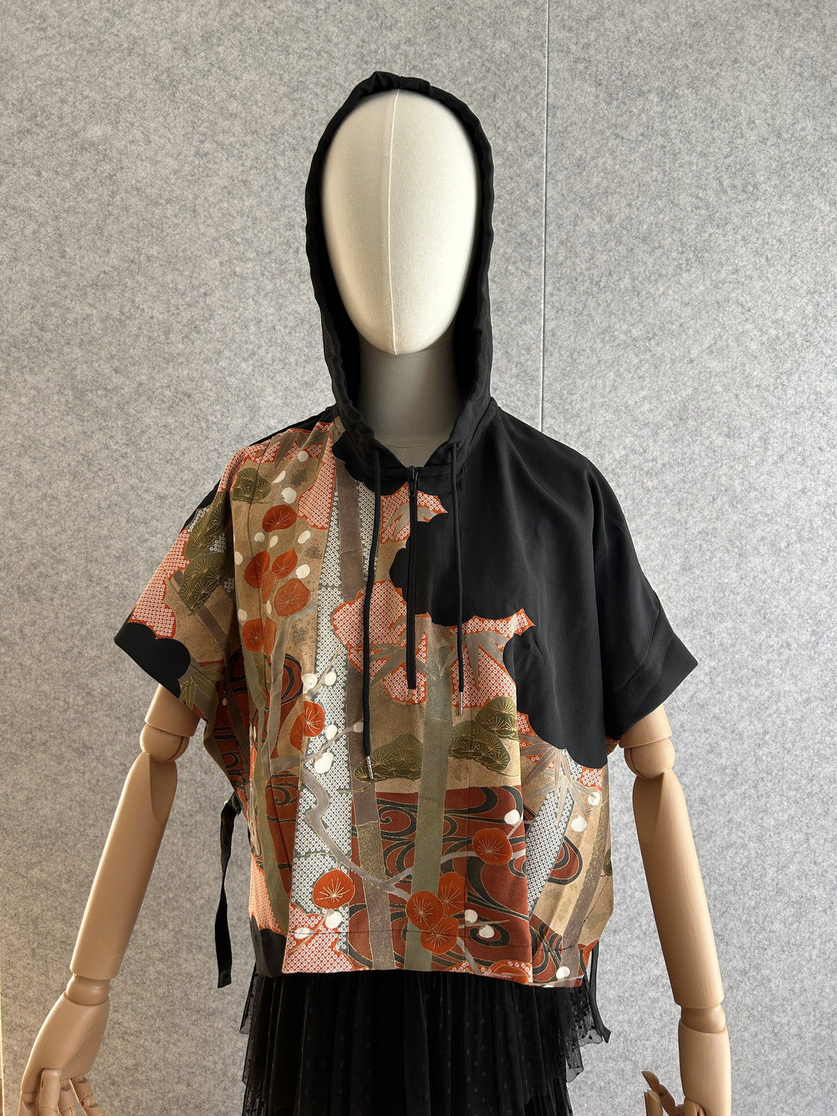 Black hooded kimono poncho with orange-red and olive tree pattern, front view