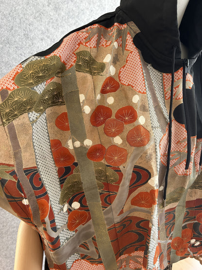 Black hooded kimono poncho, detail of orange-red and olive pattern on the shoulder