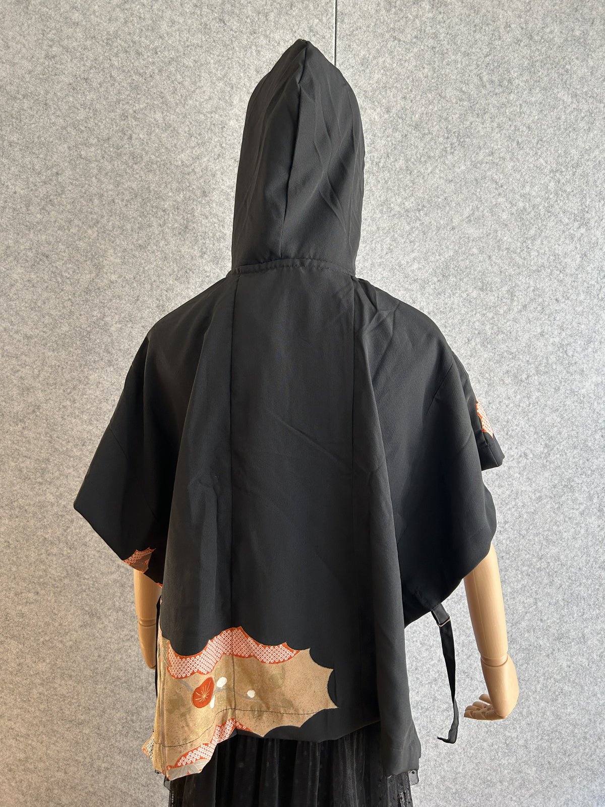 Black hooded kimono poncho with small patterned corner at the hem, back view