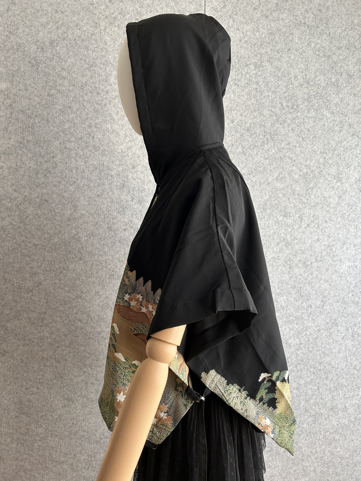 Black hooded kimono poncho with landscape pattern at the hem, side view