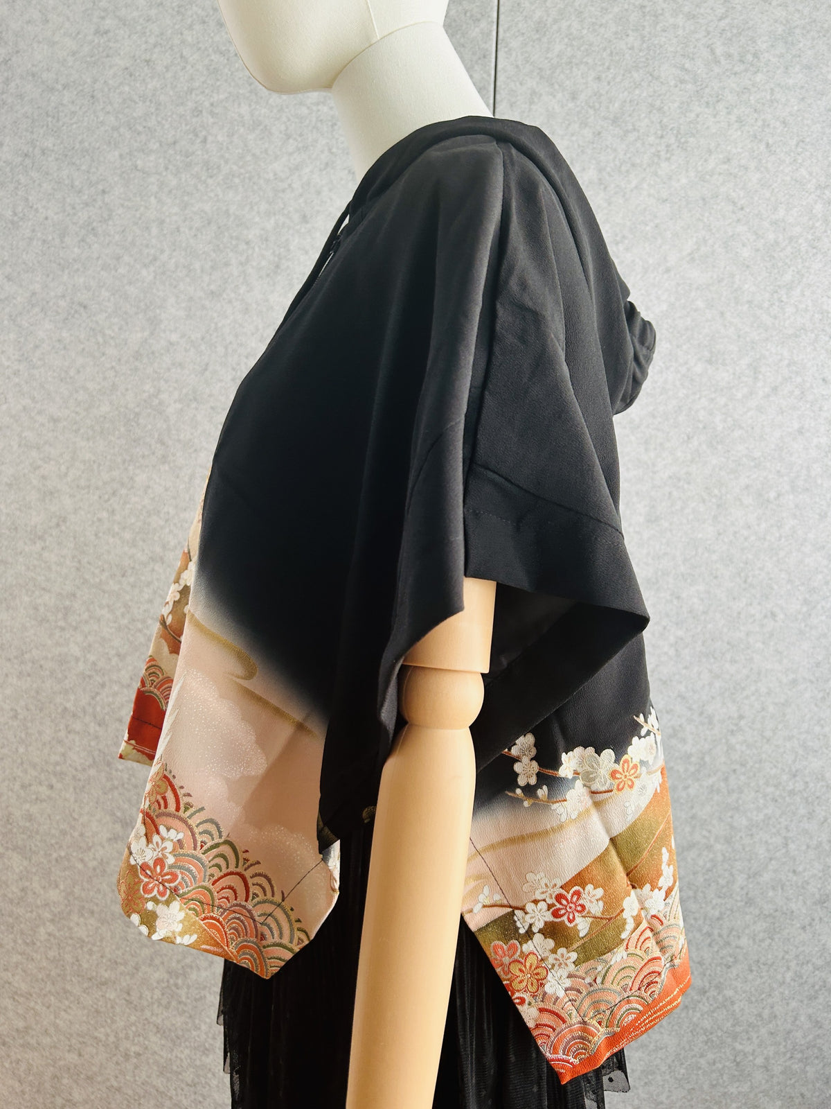 Black hooded kimono poncho with peach and orange floral hem, side view