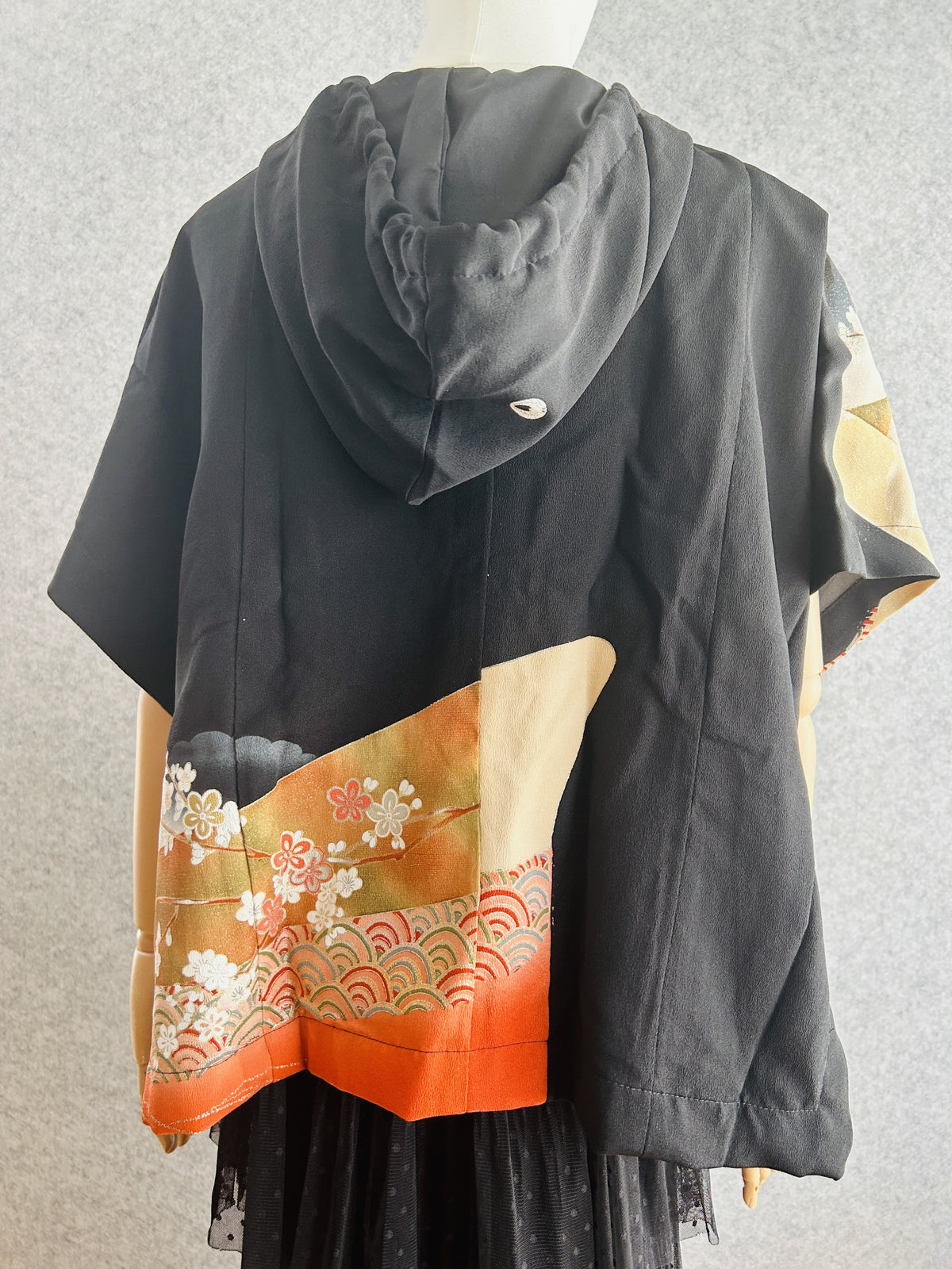 Black hooded kimono poncho with floral panel at lower left, back view