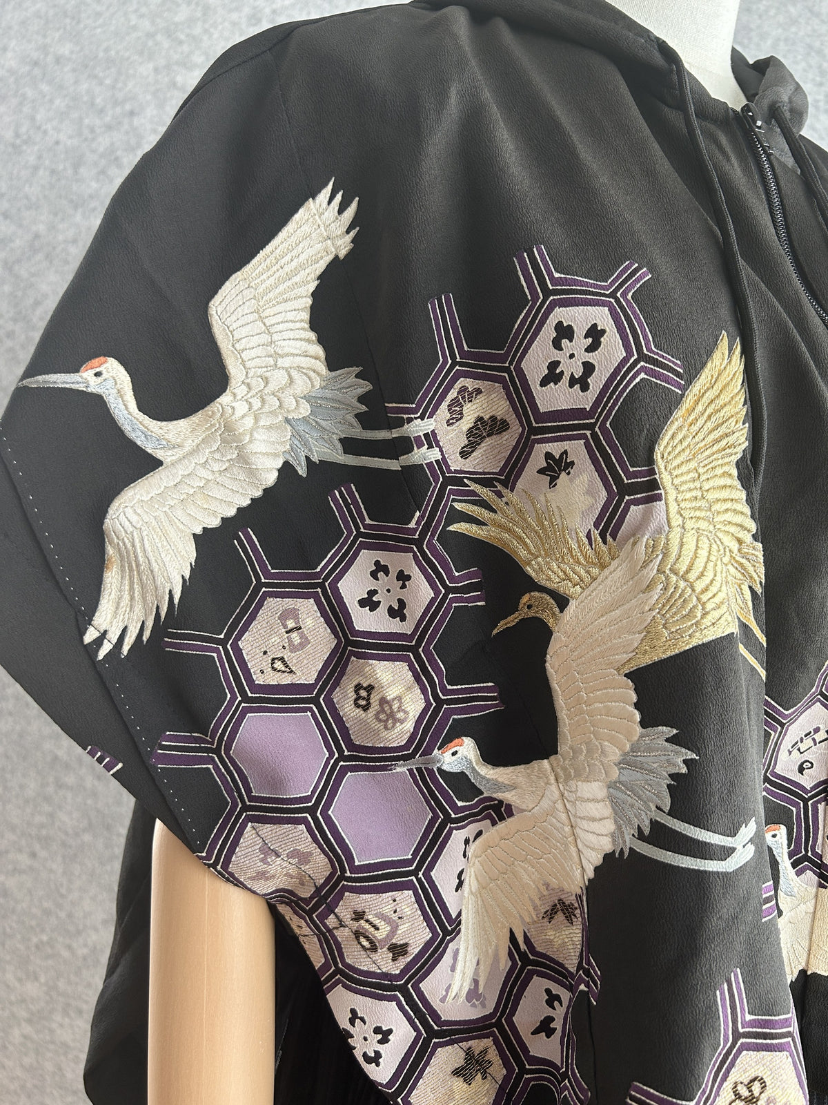 Close-up of white crane and lilac hexagon pattern on black poncho sleeve