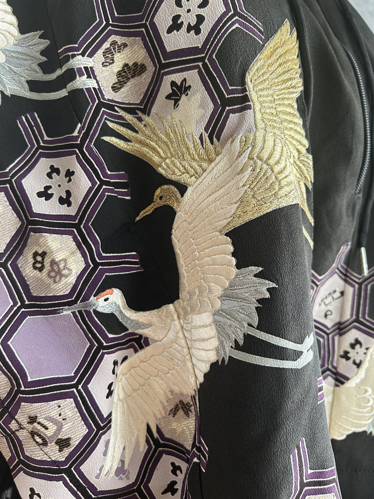Detail of gold and white embroidered-look cranes over purple hexagons