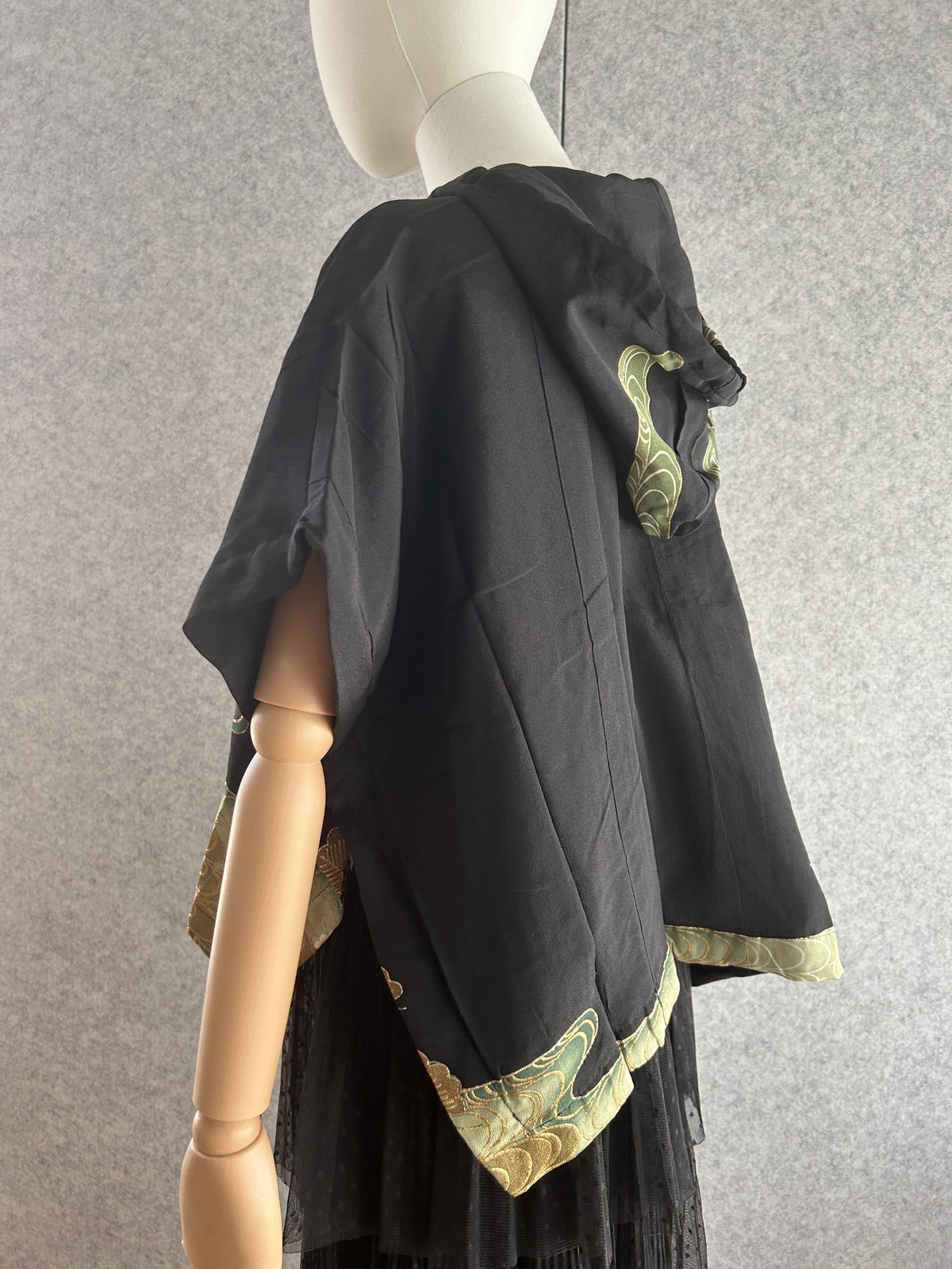 Black hooded kimono poncho with green swirl trim at hem, side back view