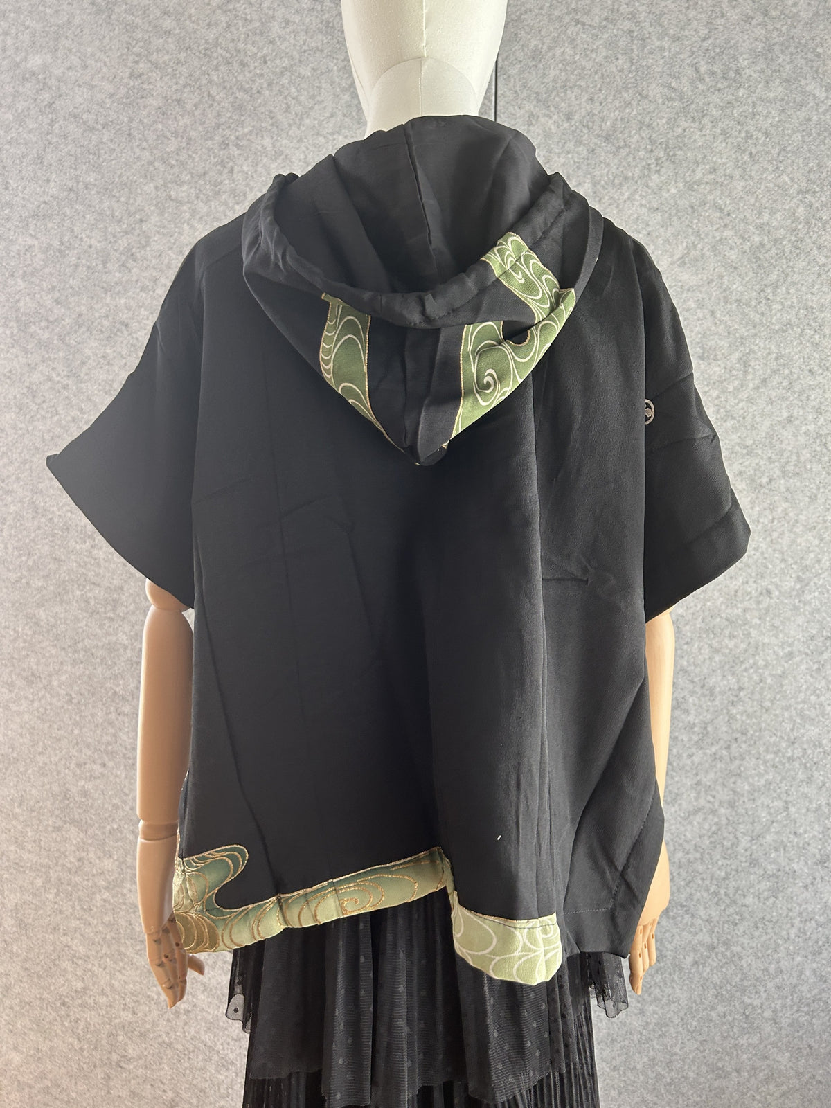Black hooded kimono poncho with green swirl hood panel and hem, back view