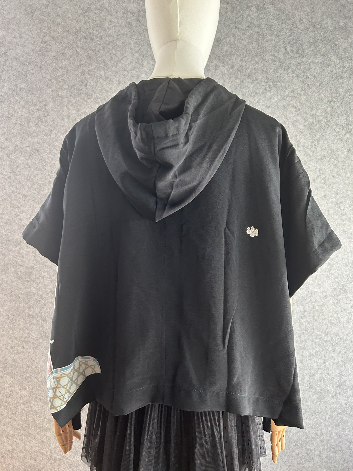 Black hooded kimono poncho with small white crest on back, back view