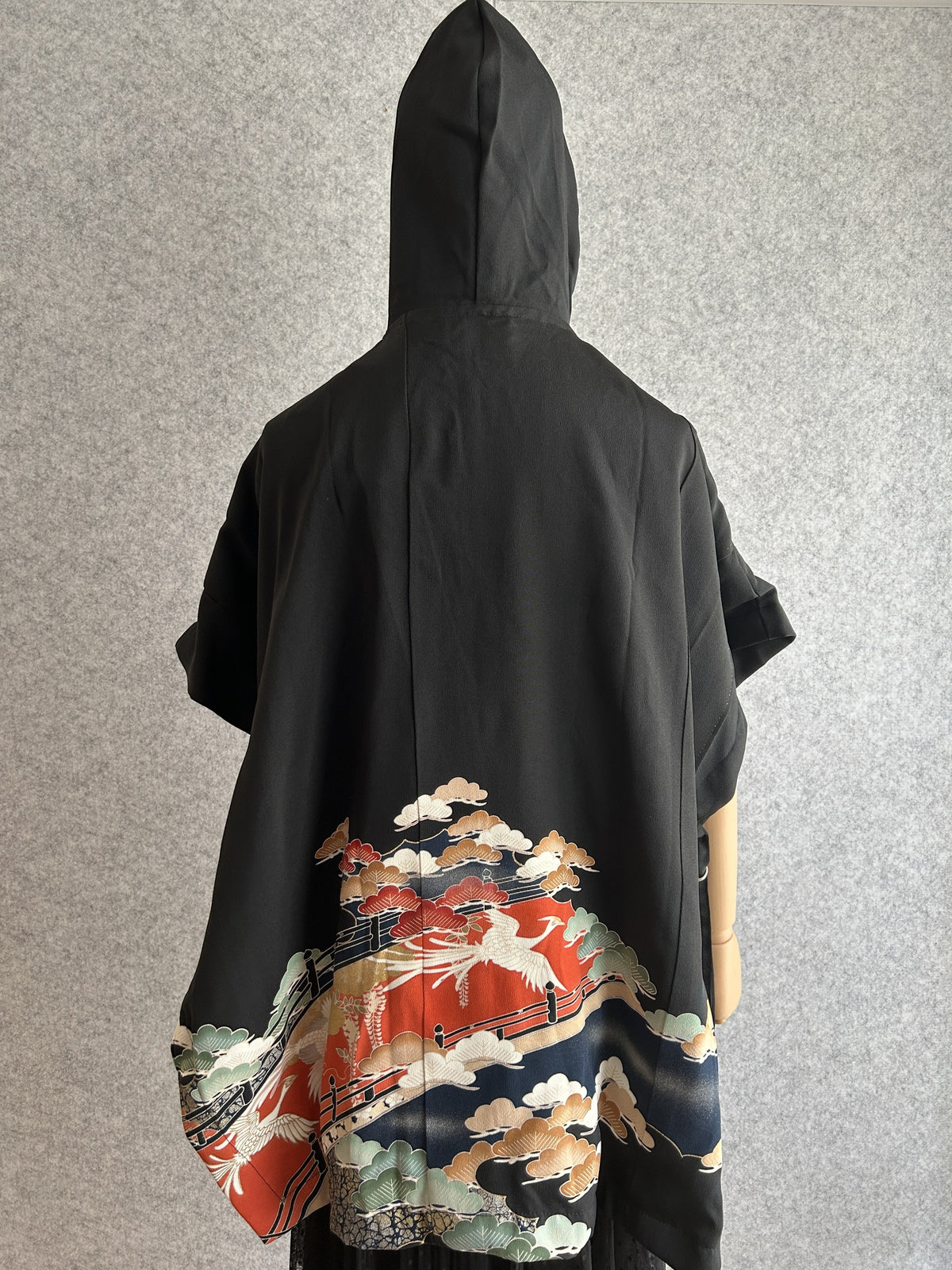 Black hooded kimono poncho with red and navy scene at the hem, back view