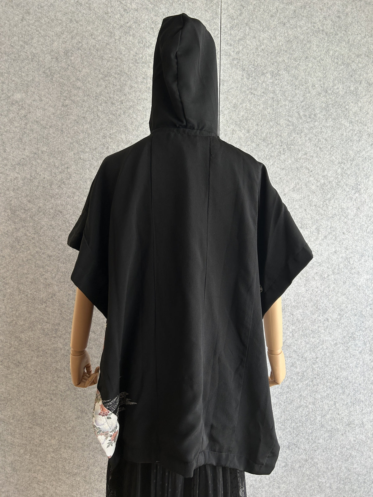 Black hooded kimono poncho with small patterned corner at the hem, back view
