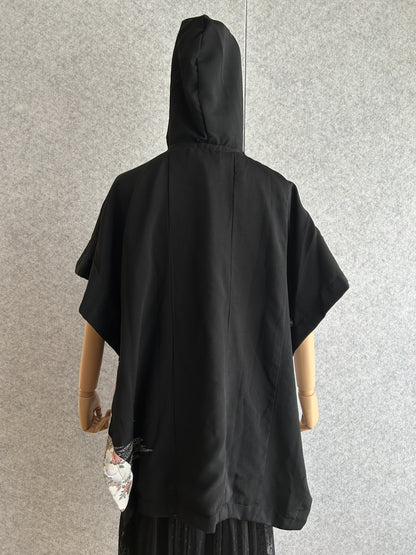Black hooded kimono poncho with small patterned corner at the hem, back view