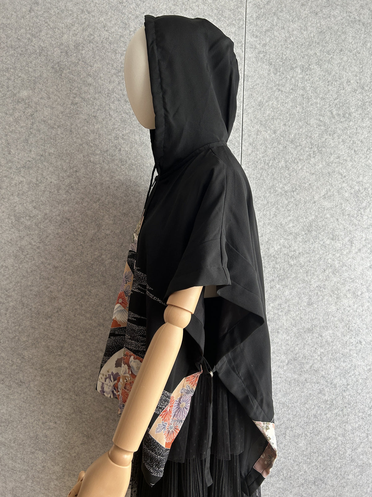 Black hooded kimono poncho with patterned front panels, side view