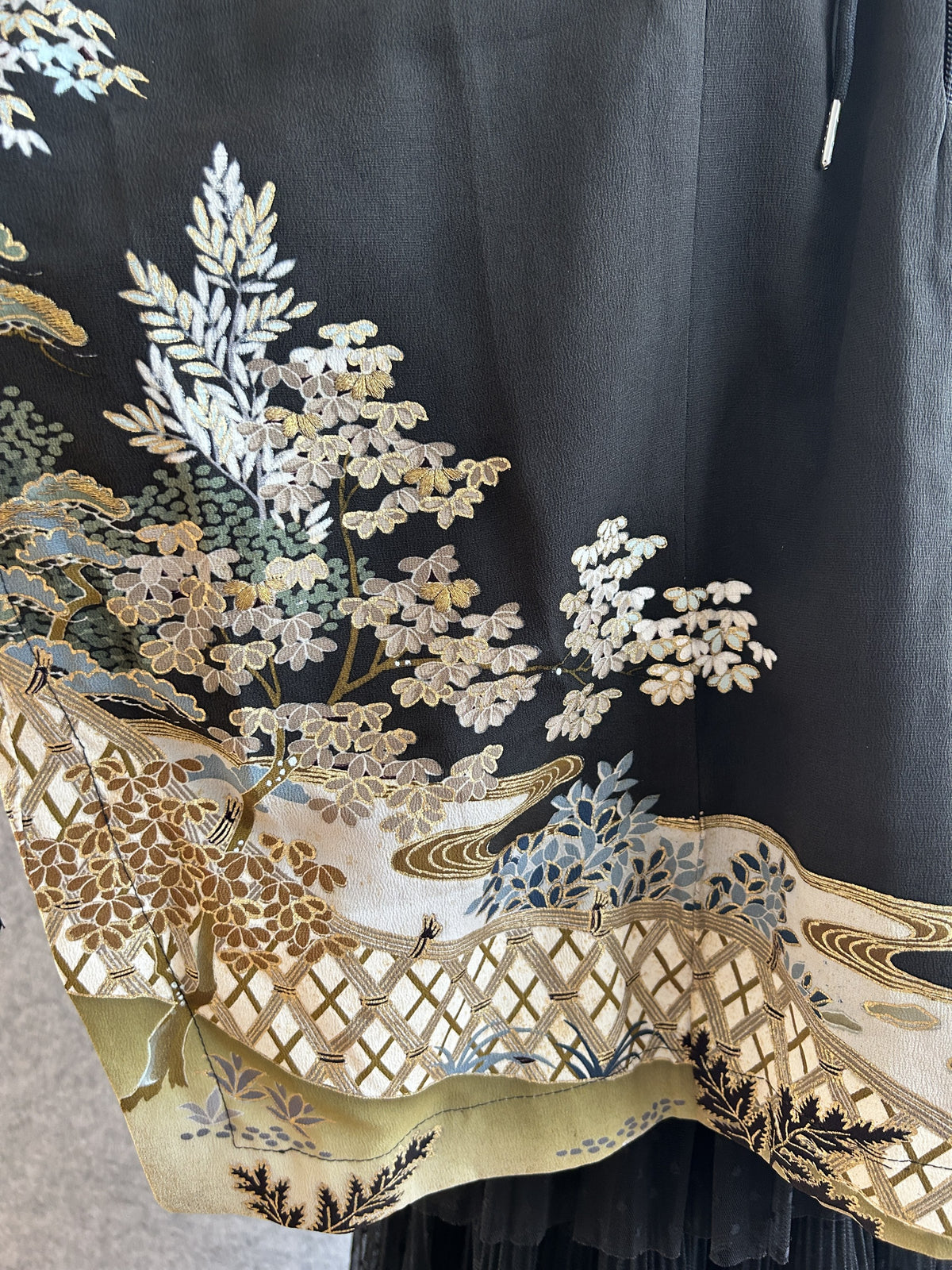 Black hooded kimono poncho, close-up of trees and lattice fence along the hem