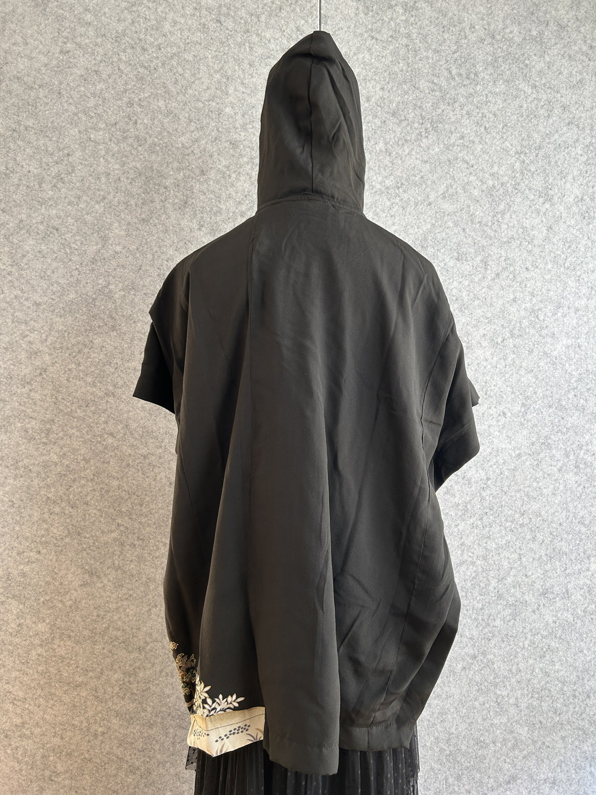 Black hooded kimono poncho with small patterned corner at the hem, back view