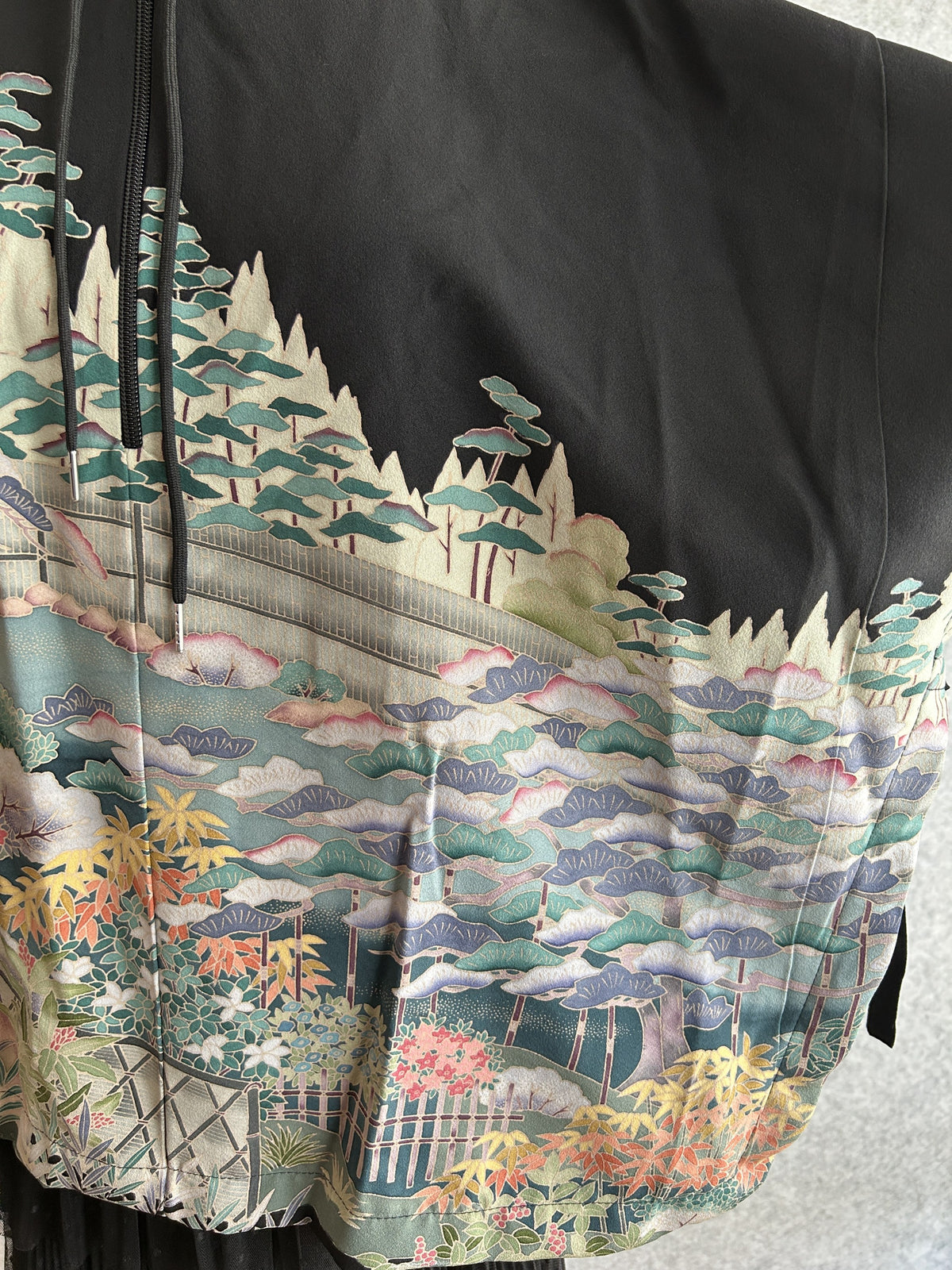 Black hooded kimono poncho, detail of garden scene with fences on the sleeve