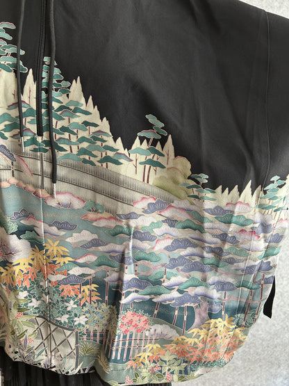 Black hooded kimono poncho, detail of garden scene with fences on the sleeve