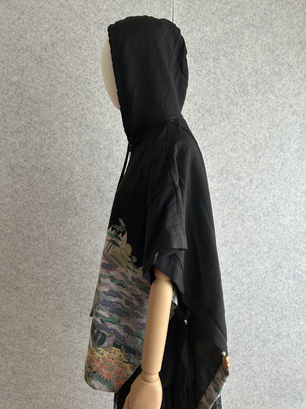 Black hooded kimono poncho with pastel pattern at the hem, side view