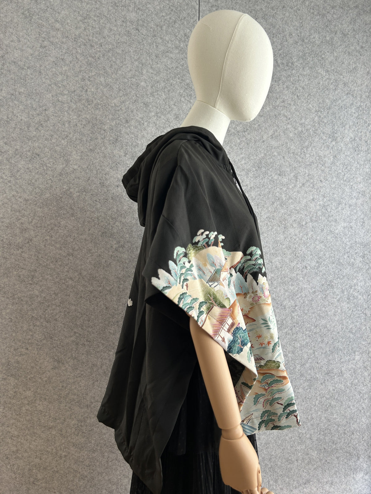 Black hooded kimono poncho with landscape pattern on the sleeve, side view with hood down