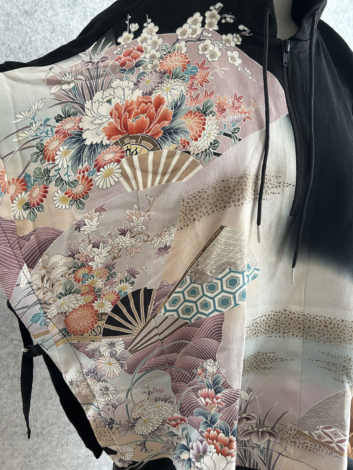 Black hooded kimono poncho, detail of front zipper, drawstring and floral fan design