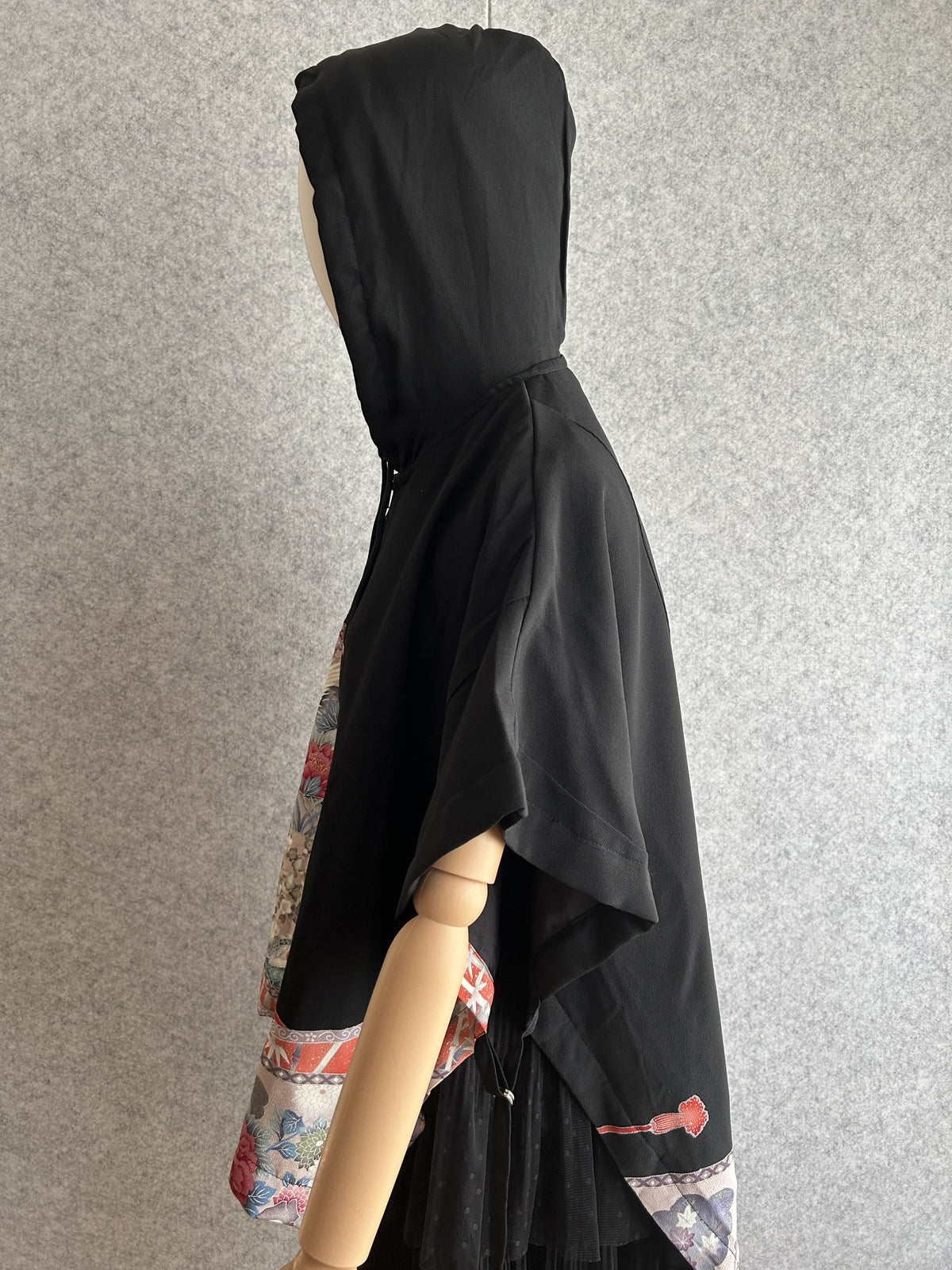 Black hooded kimono poncho with patterned lower edge, side view