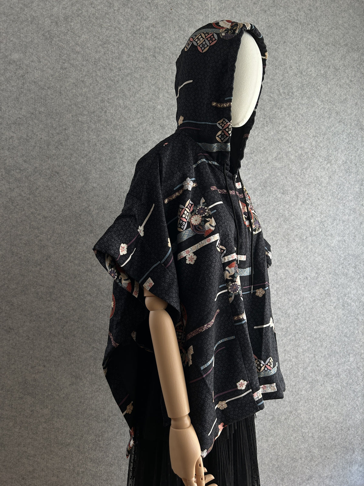 Black hooded kimono poncho with all-over ribbon and blossom pattern, side view