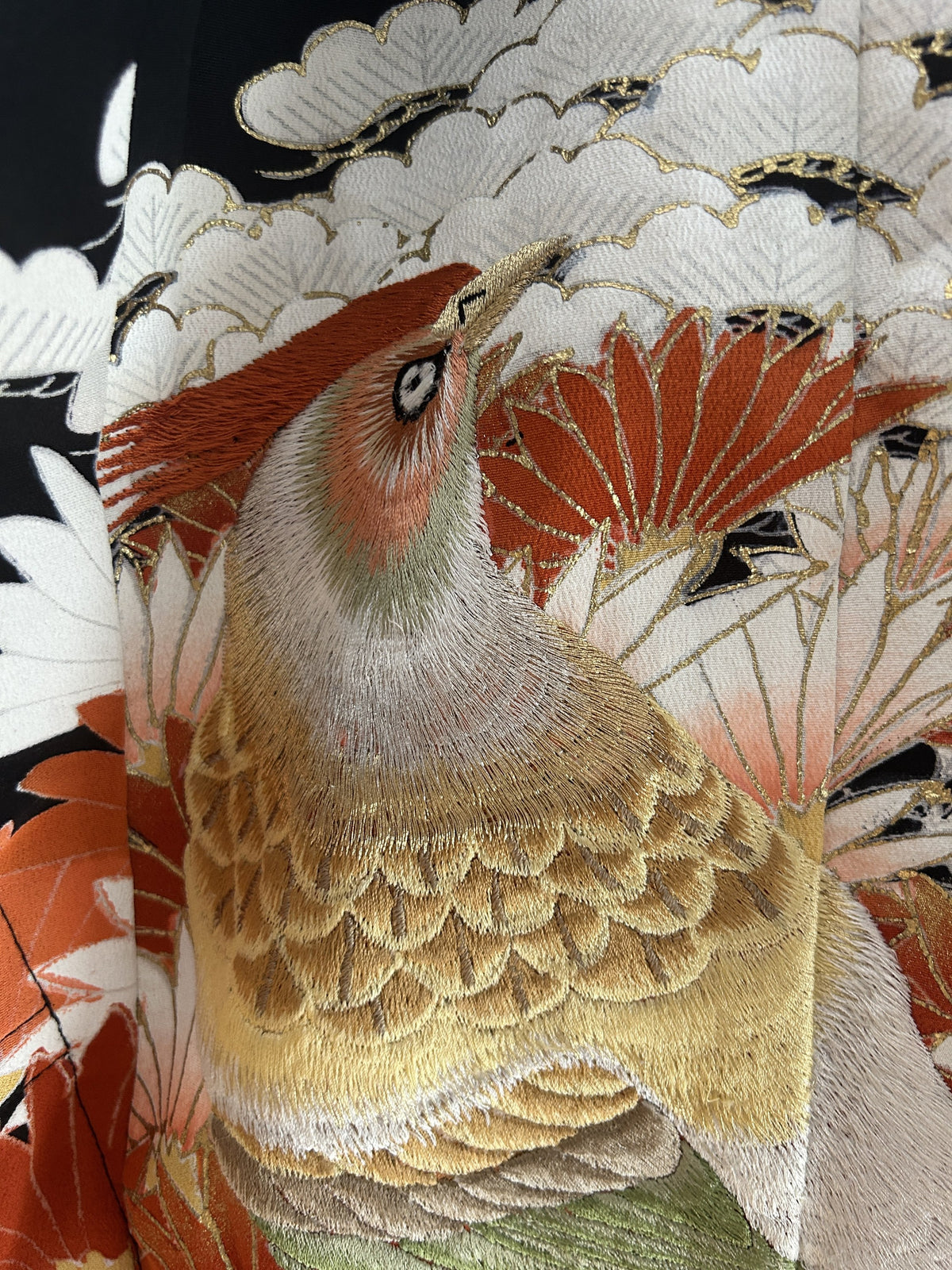 Close-up of embroidered-look bird in gold, green and orange on black poncho
