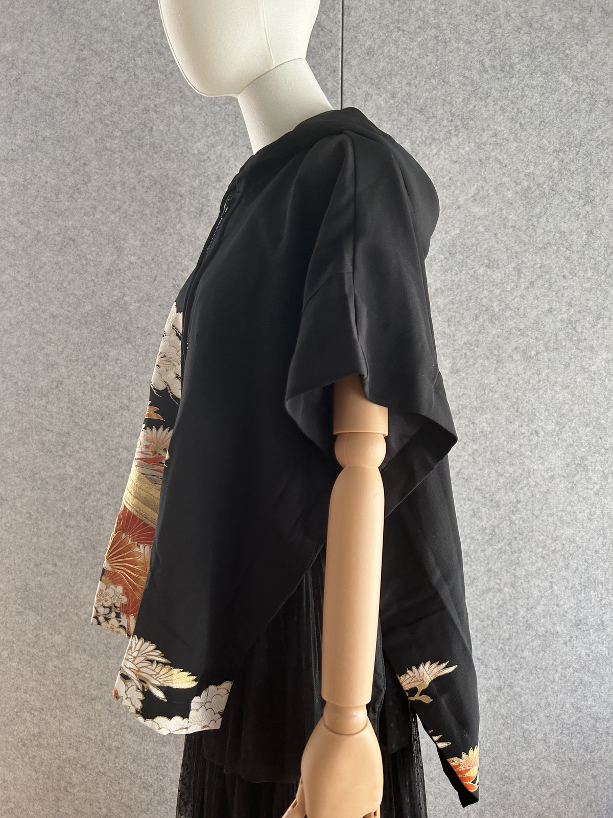 Black hooded kimono poncho with orange and white motifs at hem, side view