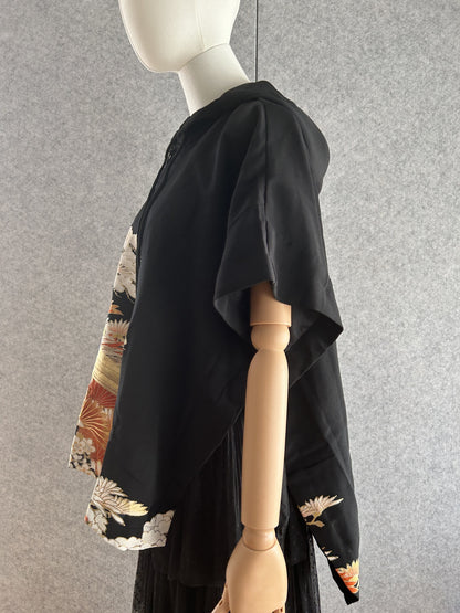 Black hooded kimono poncho with orange and white motifs at hem, side view