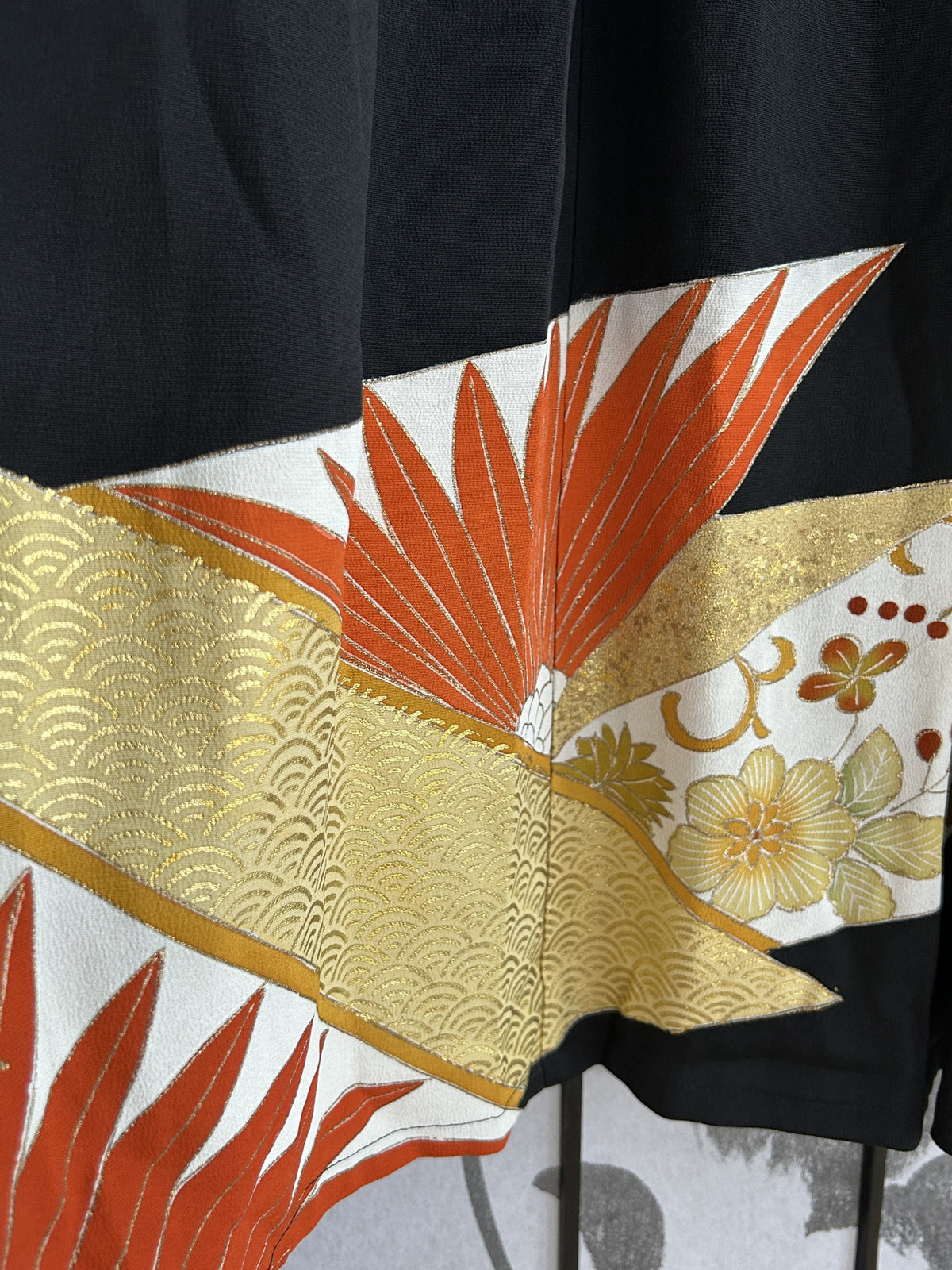 Gold wave-patterned band and orange leaves near skirt hem, detail