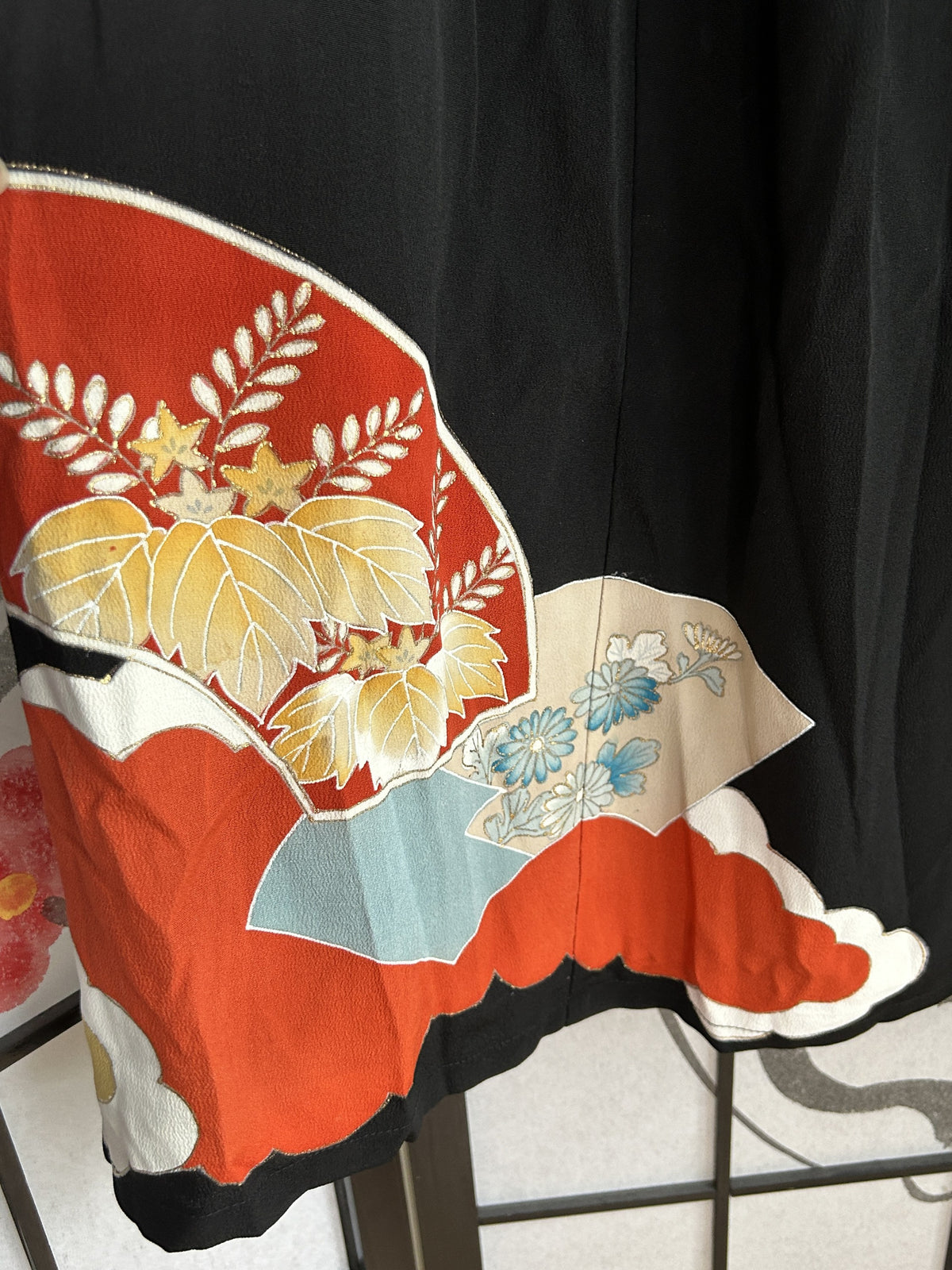 Red fan with golden leaves and blue flowers near skirt hem