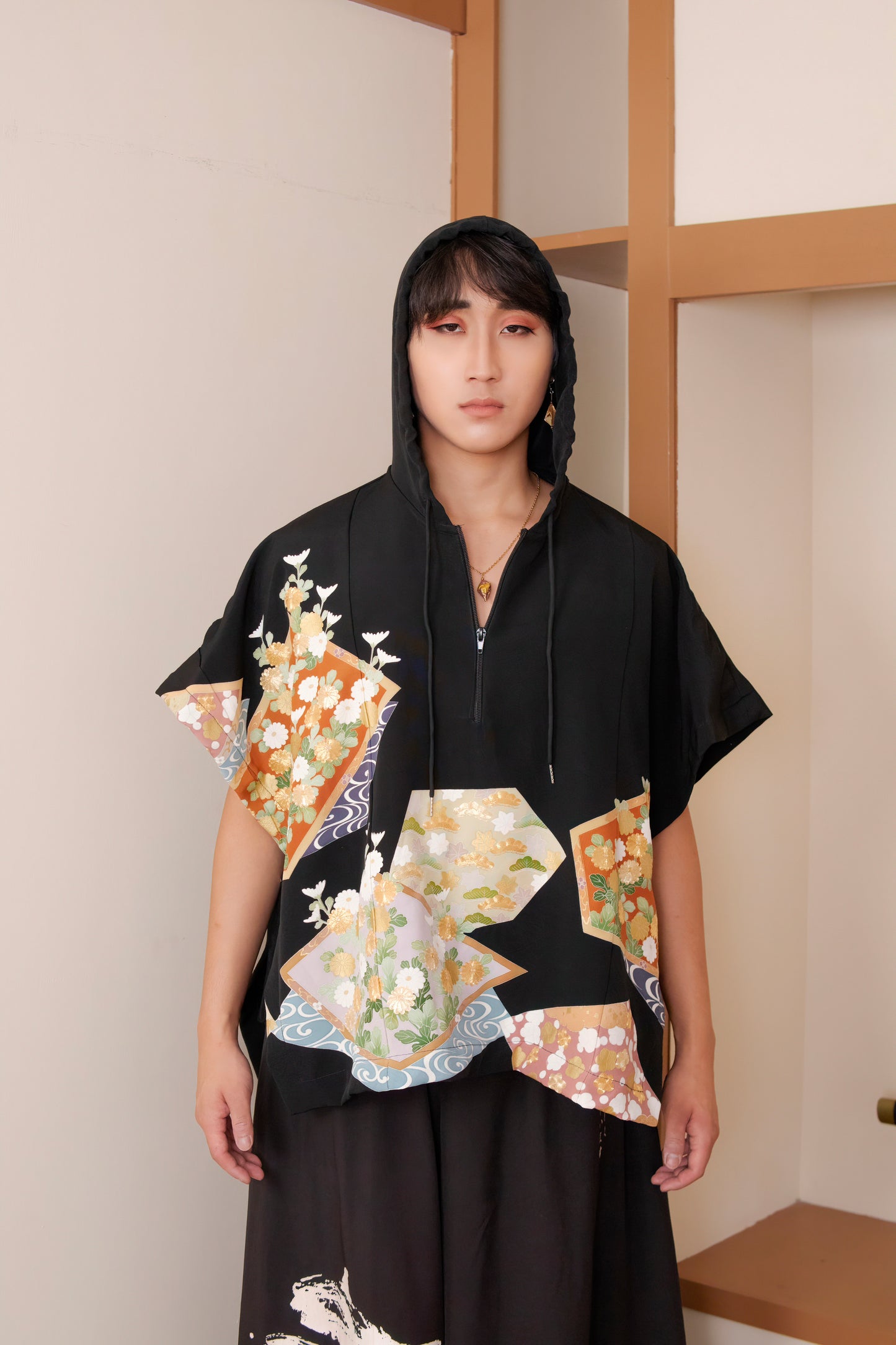 Person wearing a black kimono with colorful floral patterns in a minimal indoor setting.