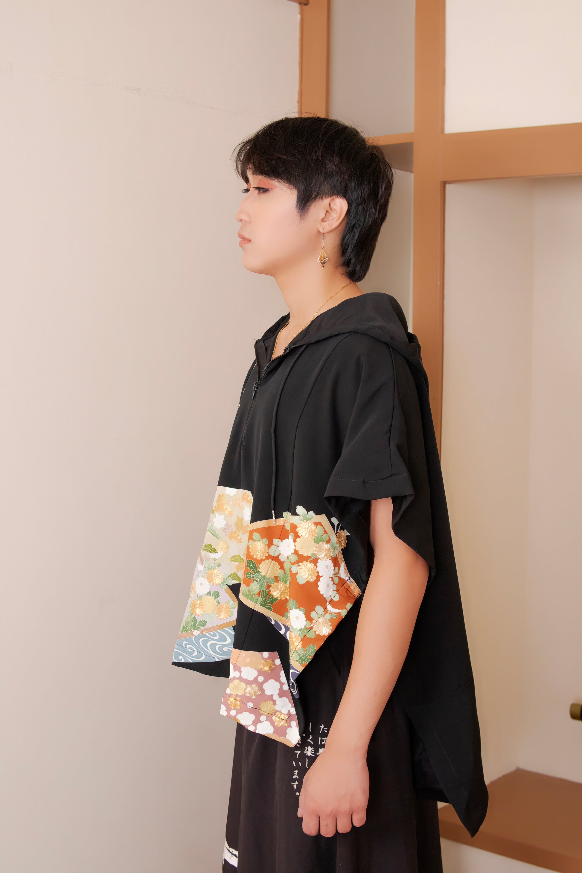 Person wearing a black outfit with floral kimono pieces draped over shoulders against a neutral background