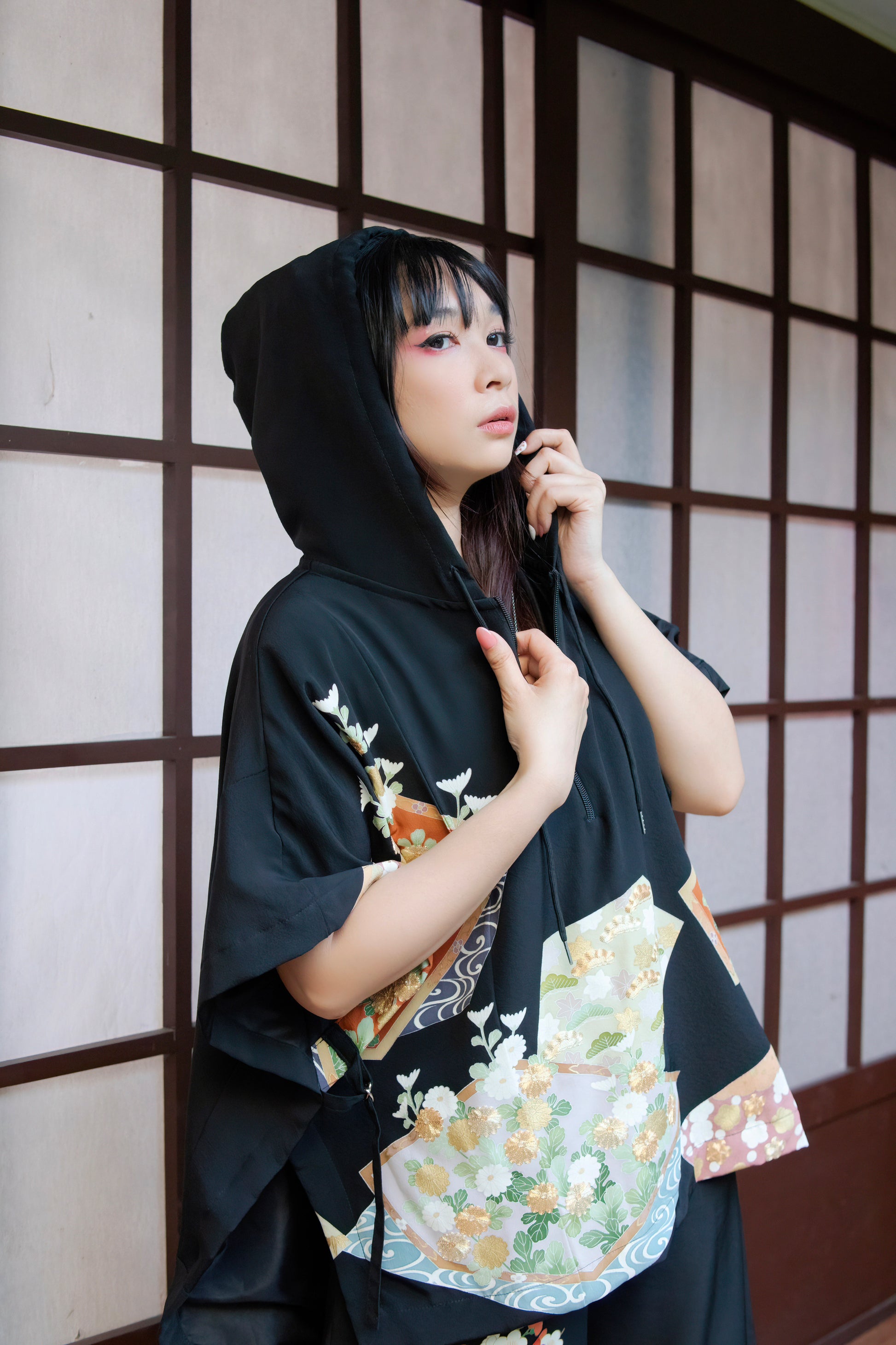 Woman wearing a black kimono with floral patterns against a wooden panel background