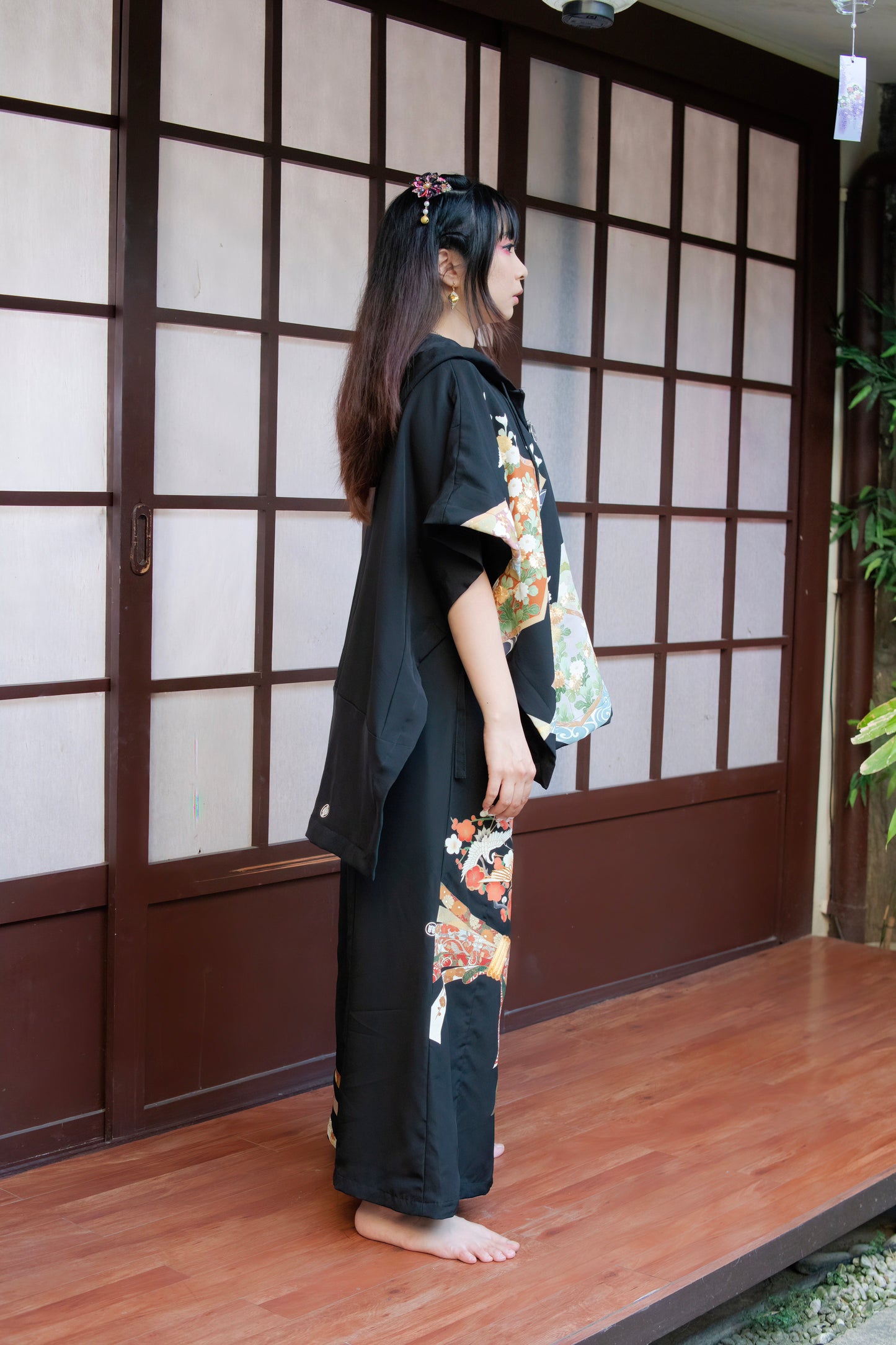 Woman wearing a black kimono with floral patterns standing in a room with wooden flooring and a shoji screen.