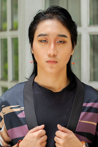 A male model wearing handmade red origami crane earrings made from chiyogami paper.
