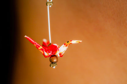 A closeup of a handmade origami crane earring made from japanese red and white chiyogami paper. 