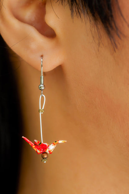 A closeup of one handmade origami crane earrings made from red and white chiyogami paper, hanging on a earlobe. 