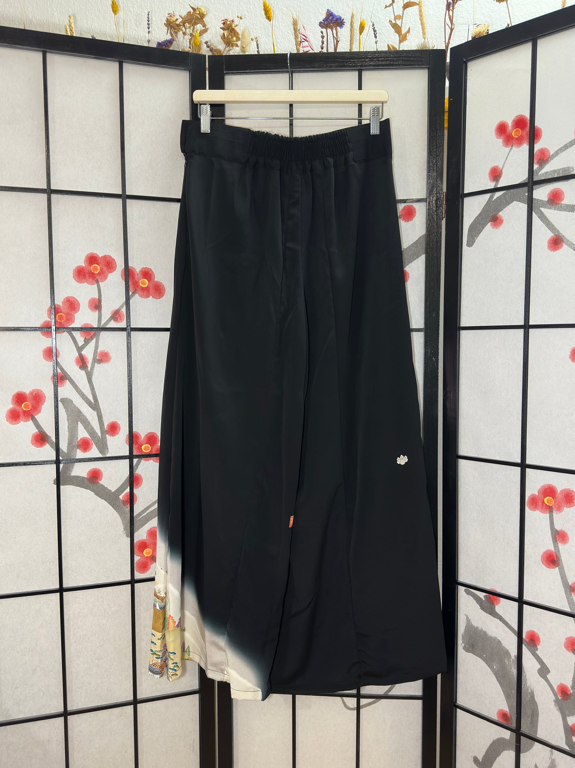 Black pants hanging on a rack against a decorative screen with floral patterns