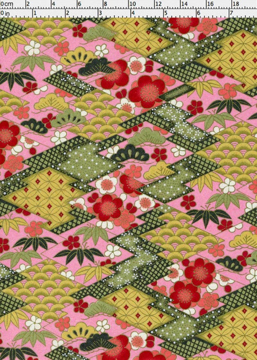 Chiyogami paper with a patchwork pattern featuring red flowers, green leaves, and geometric shapes on a pink background and a ruler for scale